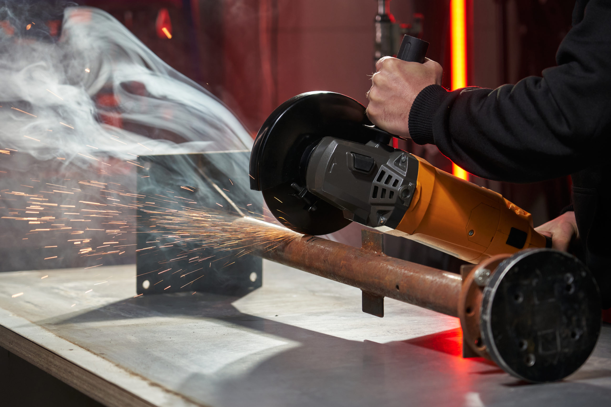 hands holding a powerful angle grinder and sawing a metal pipe on a workbench. metal emits smoke and sparks fly. High quality photo